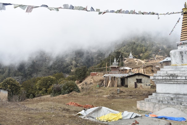 A misty morning scene showing prayer flags fluttering above a remote hillside settlement.