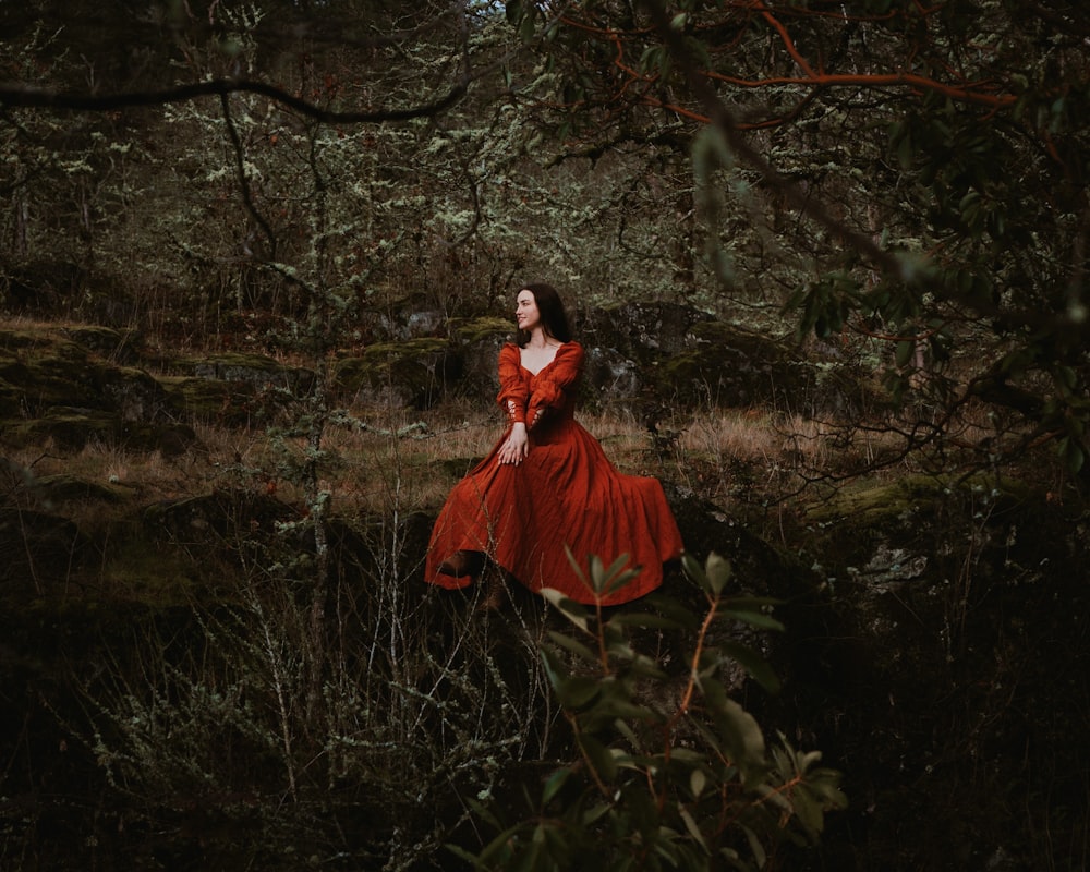 a woman in a red dress standing in a forest