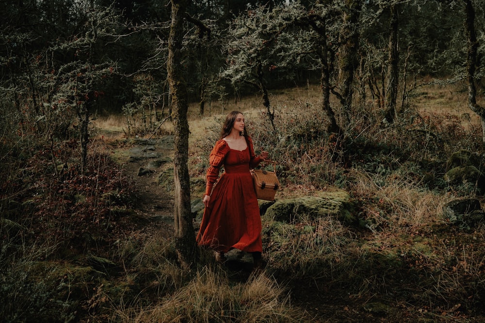 a woman in a red dress is walking through the woods