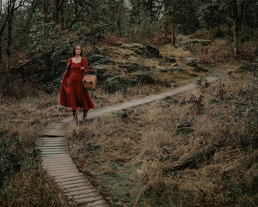 a woman in a red dress is walking through the woods