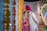 A couple dressed in traditional Indian attire partakes in a wedding ceremony. The woman is wearing a vibrant pink saree with intricate gold jewelry and vivid green blouse, while the man is dressed in an elegant white sherwani and a pink turban. They stand surrounded by garlands of marigold flowers and strings of lights, creating a festive and intimate atmosphere.