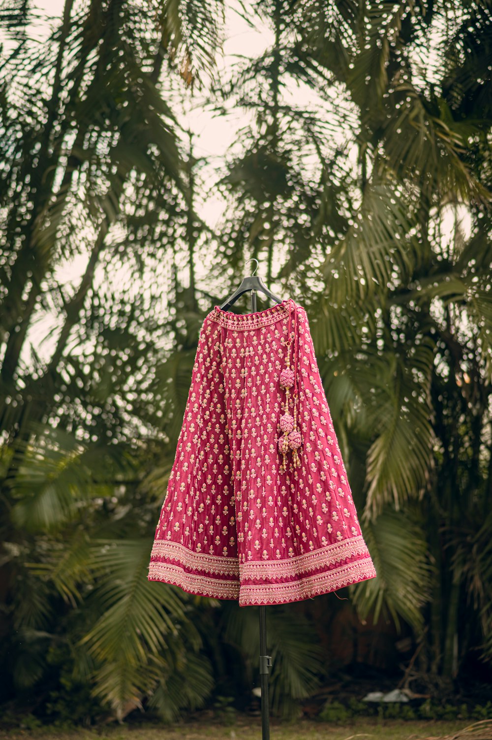 a pink and white dress on a stand in front of palm trees