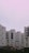 Several modern apartment buildings with a minimalist architectural design stand under a pastel pink sky. The buildings feature a combination of white and dark panels with numerous windows and small balconies.