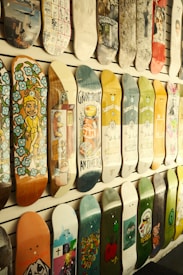 Several skateboard decks are displayed on a wall, each featuring unique and colorful designs. The designs range from abstract patterns, cartoon characters to pop art and advertisements. The decks are arranged in an orderly fashion, creating a visually appealing and artistic display.