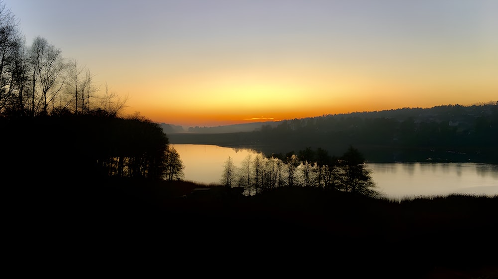 El sol se está poniendo sobre un lago con árboles en primer plano
