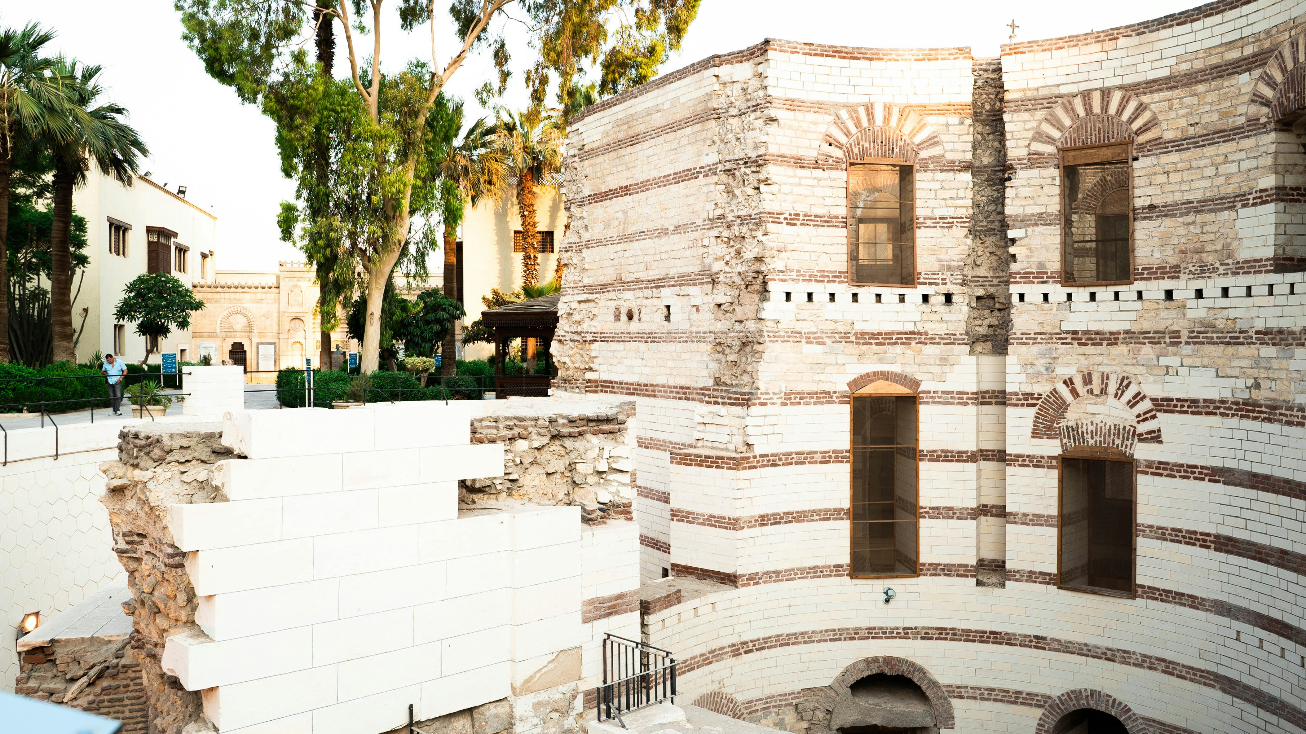 a building with a clock on the side of it, The remains of the Fortress of Babylon are visible walking the street in Coptic Cairo.