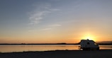 A cozy RV parked beside a serene lake at sunset, with art supplies set up outside.