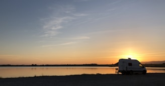 Sleek silver caravan parked beside a serene lake at sunset.