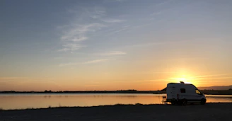 A cozy motorhome parked by a serene lake at sunset with a happy pitbull sitting at the door.