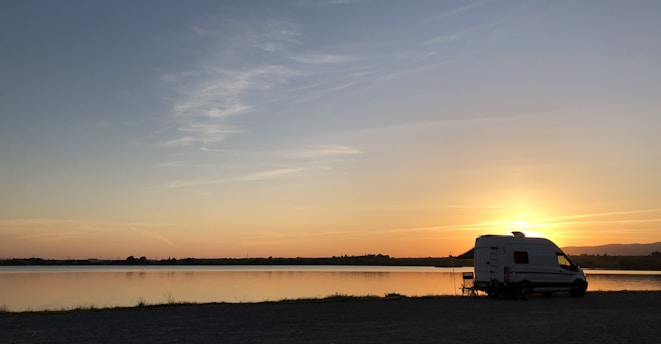 A cozy motorhome parked beside a serene lake at sunset, with bicycles leaning against it.