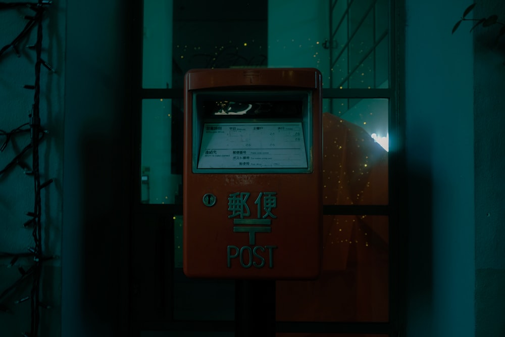 a red post box sitting in front of a window