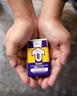 Hands holding a naloxone auto-injector device labeled Evzio, used for opioid emergencies. The device is yellow and purple with instructions for use printed on it.