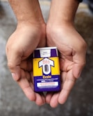Hands holding a naloxone auto-injector device labeled Evzio, used for opioid emergencies. The device is yellow and purple with instructions for use printed on it.