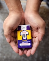 Hands holding a naloxone auto-injector device labeled Evzio, used for opioid emergencies. The device is yellow and purple with instructions for use printed on it.