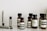 A collection of Aesop branded skincare and grooming products arranged on a light-colored marble surface. The products include small amber glass bottles with black screw caps, a tube, and stick-shaped containers. All labels are black and white, featuring product information in both English and possibly French.