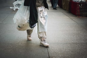 A person carrying a large cotton tote bag filled with fresh groceries outdoors.