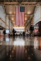 a group of people standing in a building with an american flag hanging from the ceiling