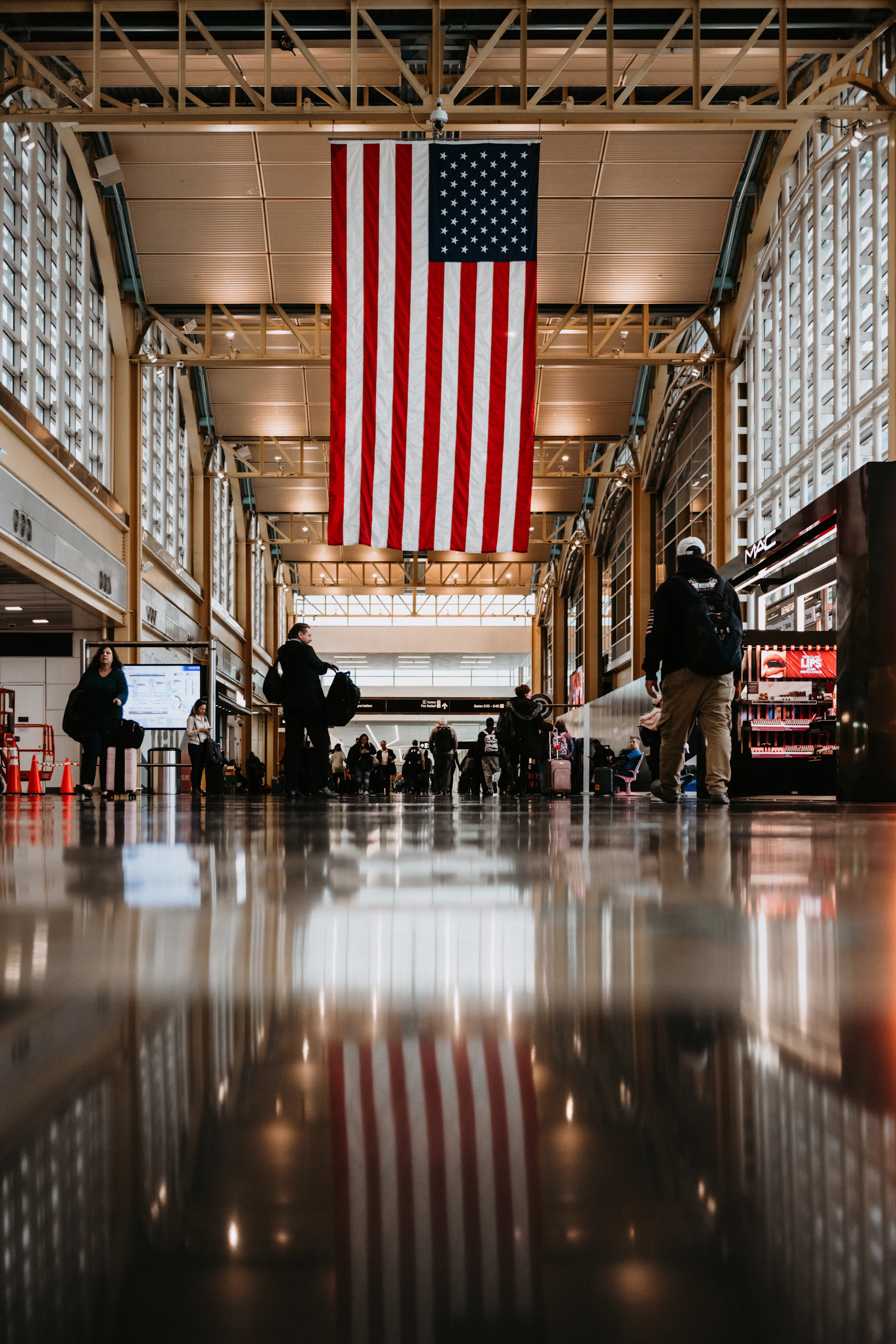 Travelers and service members under a large American flag in a transit hall.