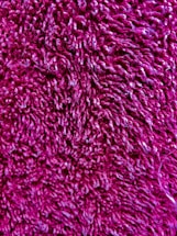 A close-up view of a textured, fuzzy material with a rich magenta color. The fibers are curly and densely packed, creating a soft appearance.