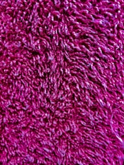 A close-up view of a textured, fuzzy material with a rich magenta color. The fibers are curly and densely packed, creating a soft appearance.