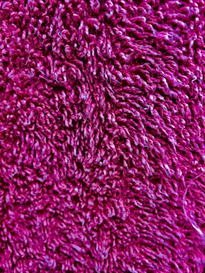 A close-up view of a textured, fuzzy material with a rich magenta color. The fibers are curly and densely packed, creating a soft appearance.