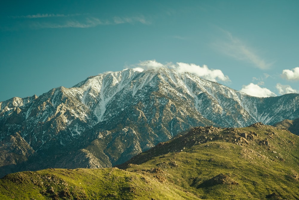 a mountain range covered in snow and green grass