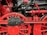 Close-up view of a red and black mechanical structure with large wheels, gears, and pipes. The intricate assembly showcases industrial engineering with detailed components and metallic textures.