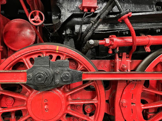 Close-up of a red and black mechanical gear with engineering blueprints in the background.