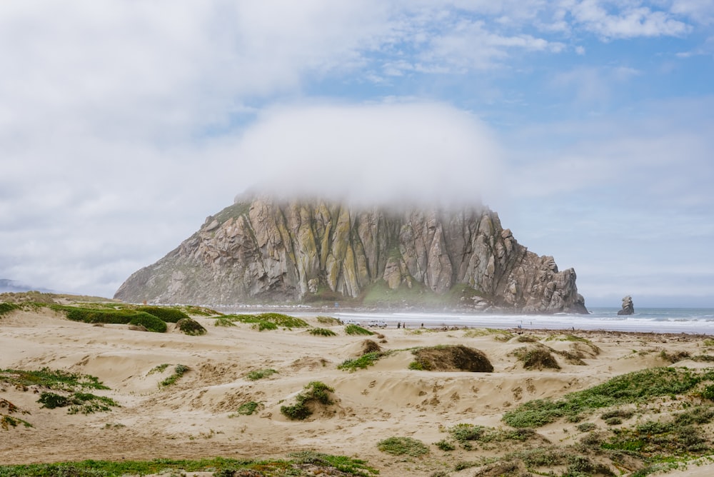 a large rock sticking out of the ocean next to a sandy beach