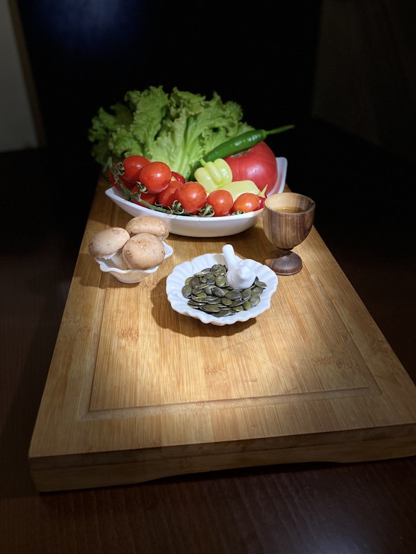 a wooden cutting board topped with a bowl of vegetables