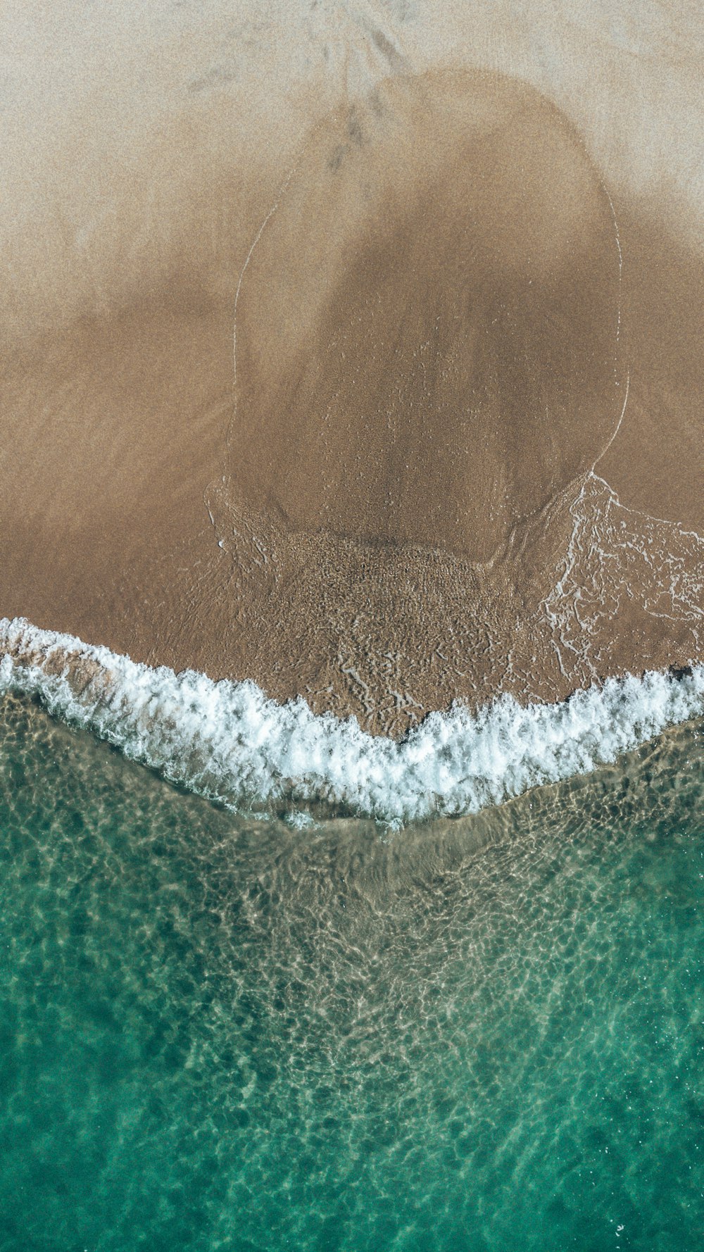 an aerial view of a beach with a wave coming in