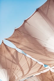 Large, beige canvas structures with metal fixtures support the sails against a clear blue sky. The sun casts deep shadows and highlights the texture of the fabric.