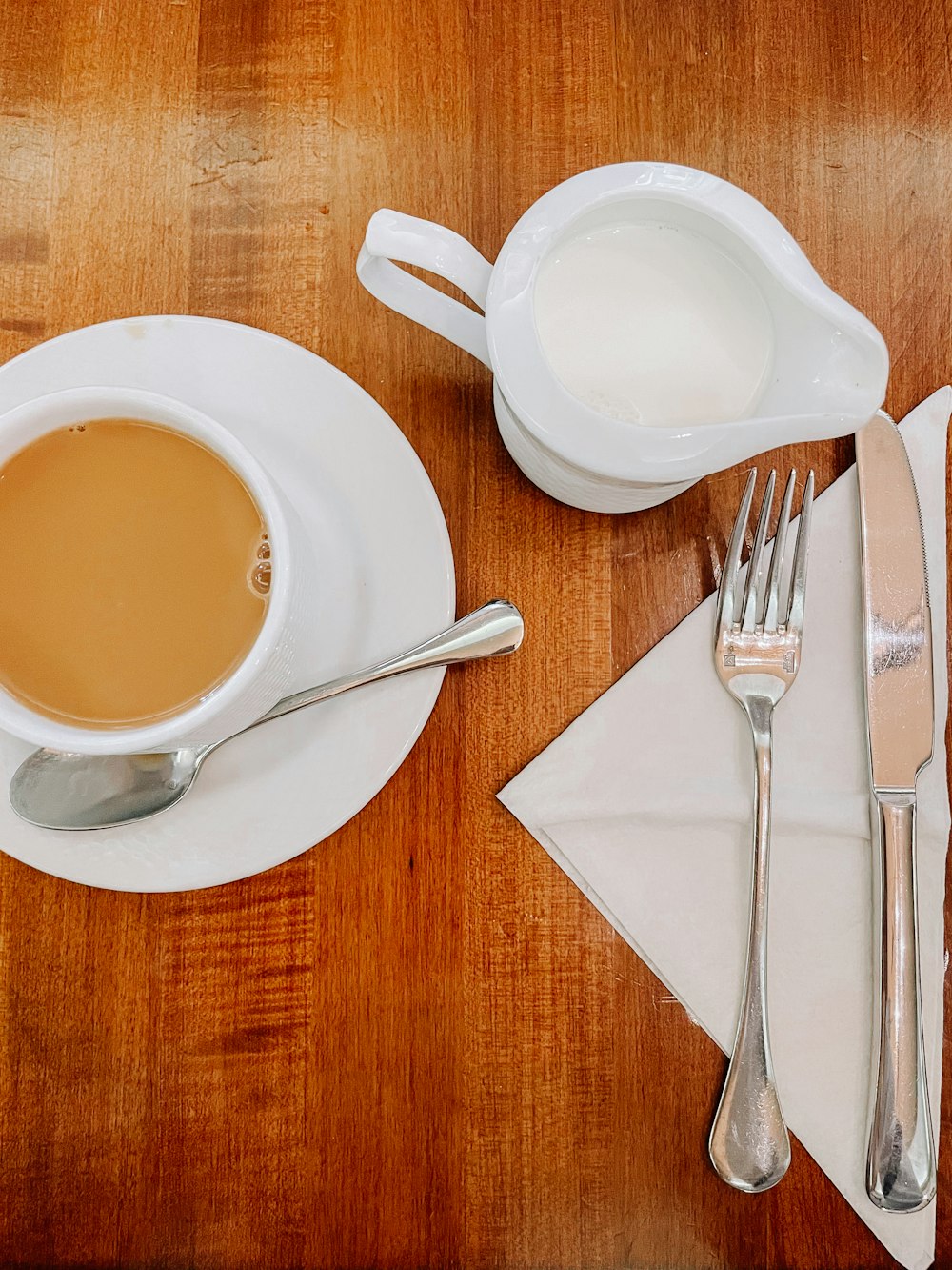 a wooden table topped with a cup of coffee and silverware