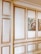 An interior wall featuring elaborate paneling with raised moldings, painted in white and golden hues. Two framed paintings of birdcages and birds are hung side by side on the wall. The style exudes a classic and sophisticated look.
