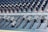 A close-up view of an audio mixing console with various sliders and knobs arranged in rows. The equipment appears complex, used for adjusting sound levels and mixing audio. The sliders are positioned at different levels, suggesting active sound management.