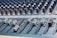 A close-up view of an audio mixing console with various sliders and knobs arranged in rows. The equipment appears complex, used for adjusting sound levels and mixing audio. The sliders are positioned at different levels, suggesting active sound management.