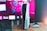 A gaming console is placed on a wooden table with a game controller nearby. In the background, a television screen displays colorful graphics, including geometric shapes and vibrant colors.