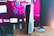 A gaming console is placed on a wooden table with a game controller nearby. In the background, a television screen displays colorful graphics, including geometric shapes and vibrant colors.
