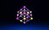 A geometric structure composed of multicolored spheres connected by lines, forming a three-dimensional lattice against a dark background.