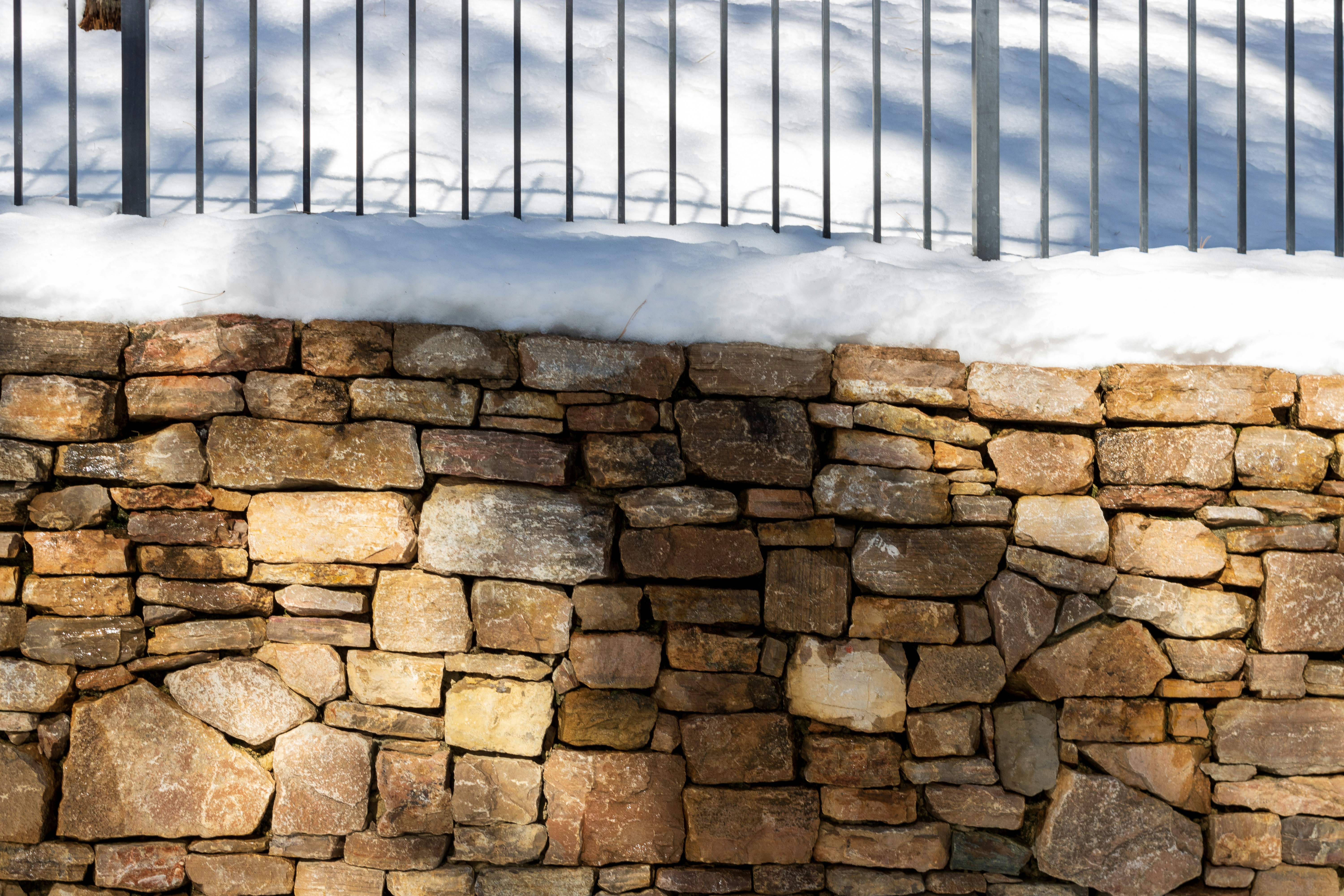 a stone wall covered in snow next to a fence