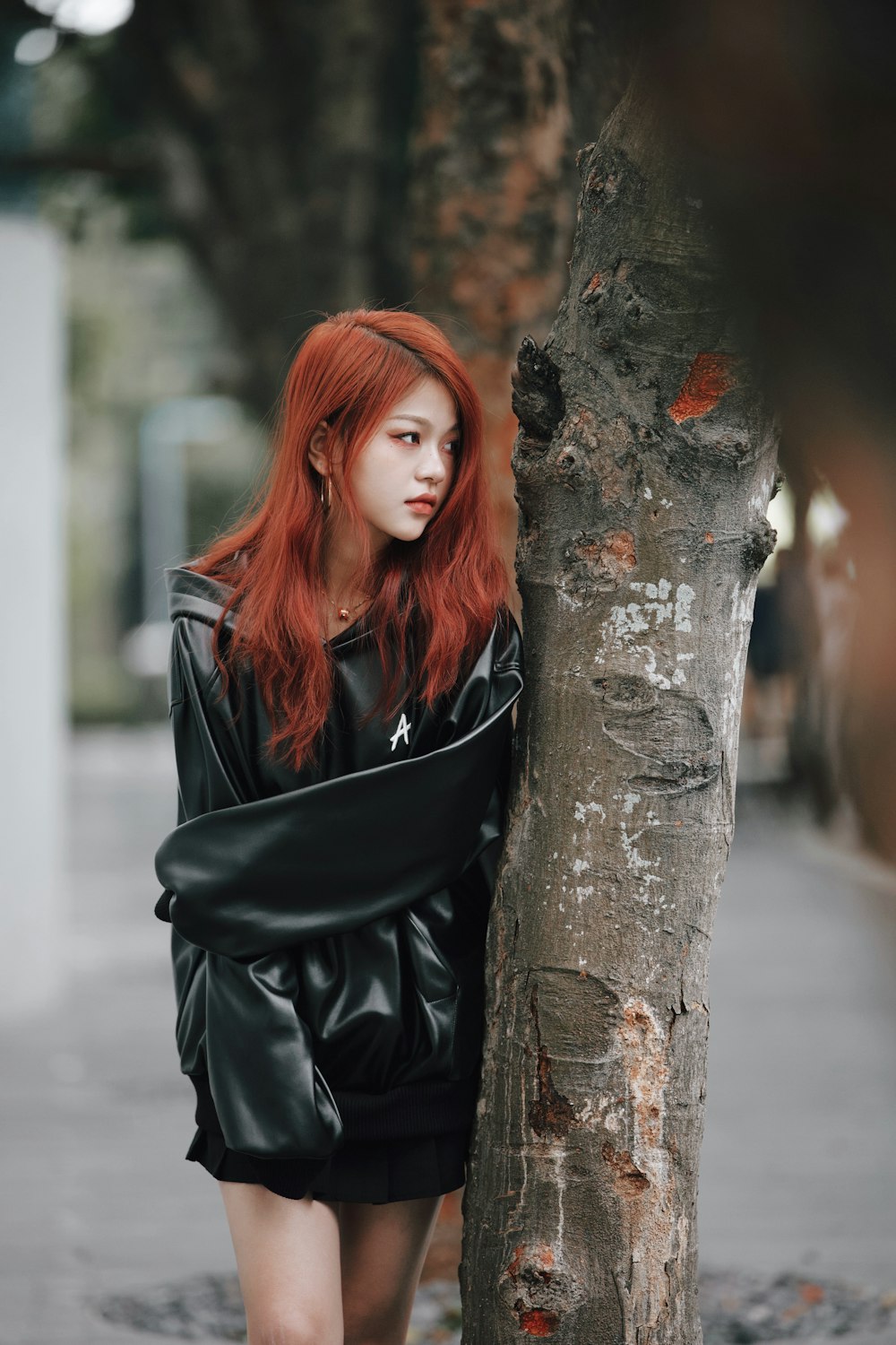a woman with red hair leaning against a tree