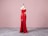 A red sequined evening gown is displayed on a dress form against a pale pink background. The gown is floor-length with a side slit and features an asymmetric neckline with one strap over the shoulder and a cutout near the waist.