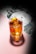 A beautifully crafted cocktail sits in a clear glass with large ice cubes and an elegant twist of lemon peel on top. The drink has a rich amber color, and the glass casts a shadow on a soft pink surface. In the background, there is a floral pattern featuring white flowers and green leaves, creating a sophisticated and artistic ambiance.