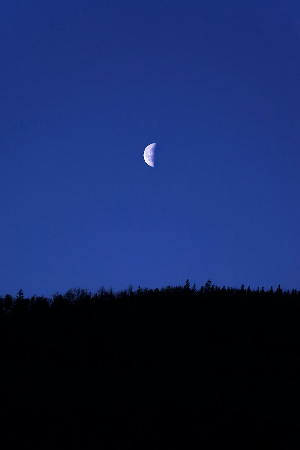 a half moon is seen in the sky above a hill