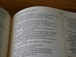 An open book displaying text with clear, black print on white pages. The visible text includes a heading titled 'The Books of the Prophets' followed by a passage containing various lines and verses. The pages have a gently curved appearance, indicative of being naturally open. The background is a wooden surface, suggesting the book is resting on a table.