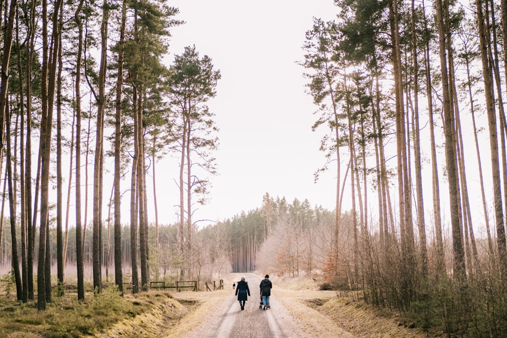 two people walking down a dirt road in the woods