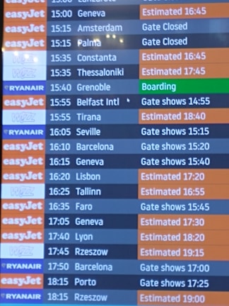 A flight departure board displaying various airlines and their scheduled flights. The board shows destinations, companies such as EasyJet, Ryanair, and Wizz, departure times, and status updates like 'Gate Closed', 'Estimated', or 'Boarding'. The background color for EasyJet is orange, Ryanair is blue, and Wizz is purple, with corresponding flight status updates in different colors.