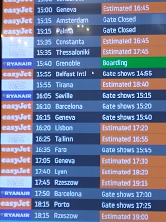 A flight departure board displaying various airlines and their scheduled flights. The board shows destinations, companies such as EasyJet, Ryanair, and Wizz, departure times, and status updates like 'Gate Closed', 'Estimated', or 'Boarding'. The background color for EasyJet is orange, Ryanair is blue, and Wizz is purple, with corresponding flight status updates in different colors.
