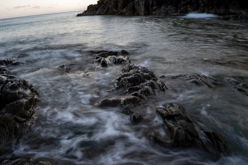 Rocky shoreline bathed in gentle evening light, waves lapping quietly.