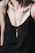 A person wearing a black spaghetti strap top is adorned with a necklace featuring a gold pendant in a unique design. The necklace has a sleek, modern aesthetic, adding elegance to the overall look.